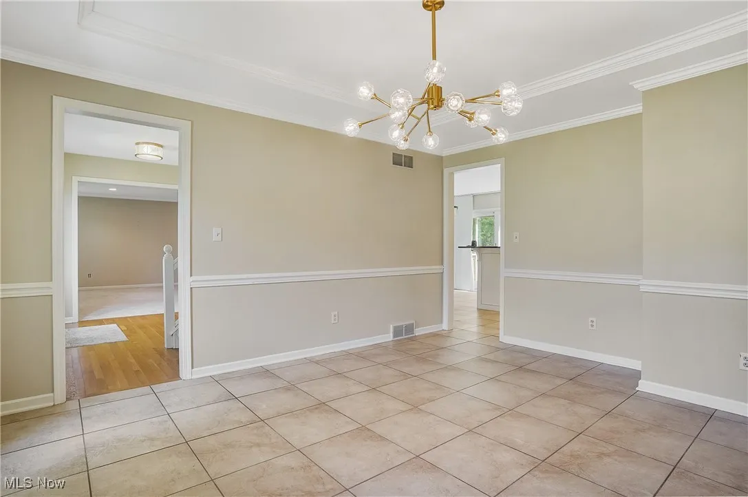 Spare room with ornamental molding, light tile patterned floors, a chandelier, and a tray ceiling
