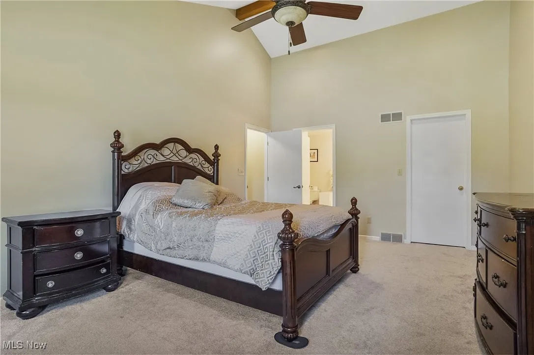 Carpeted bedroom with high vaulted ceiling, connected bathroom, and a ceiling fan