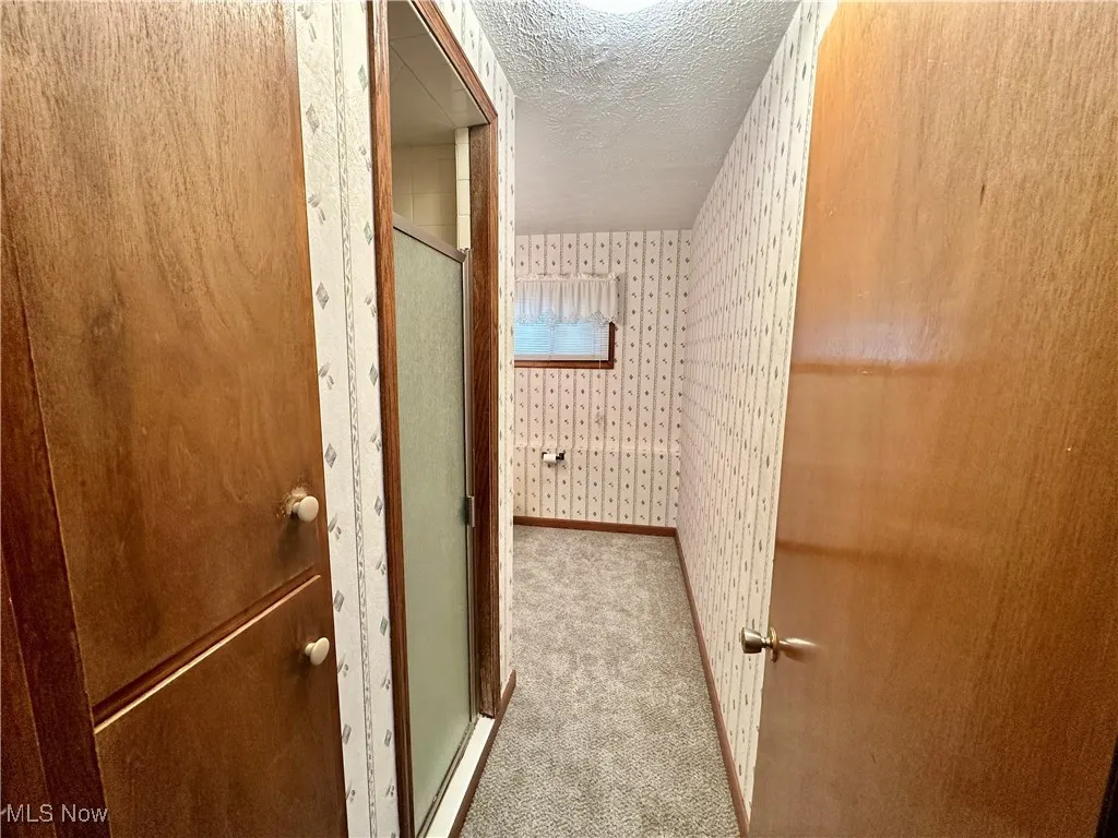 Full bath with wallpapered walls, a stall shower, and a textured ceiling