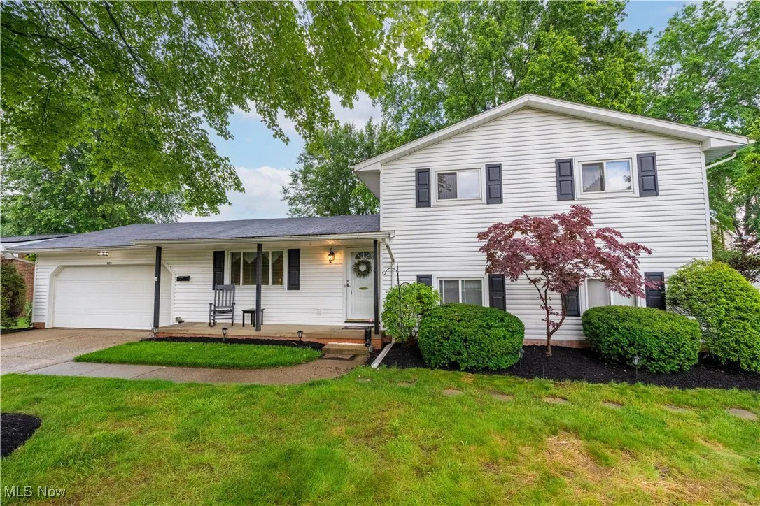 Split level home with an attached garage, covered porch, concrete driveway, and a front yard