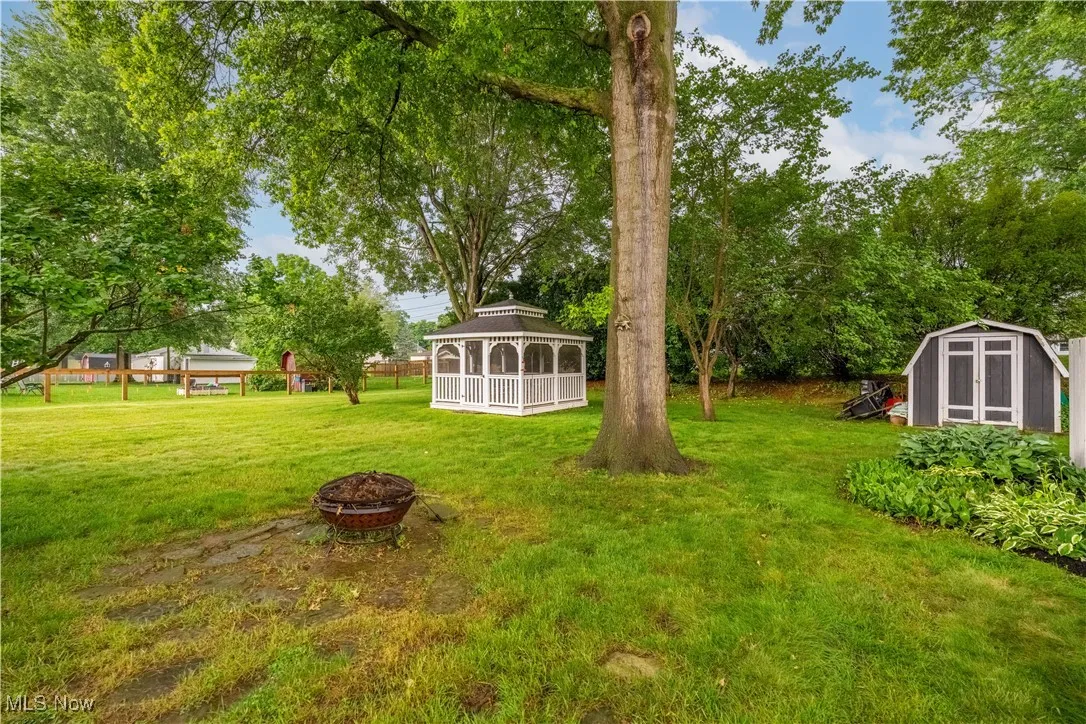 View of green lawn featuring a gazebo, an outdoor fire pit, and a storage shed
