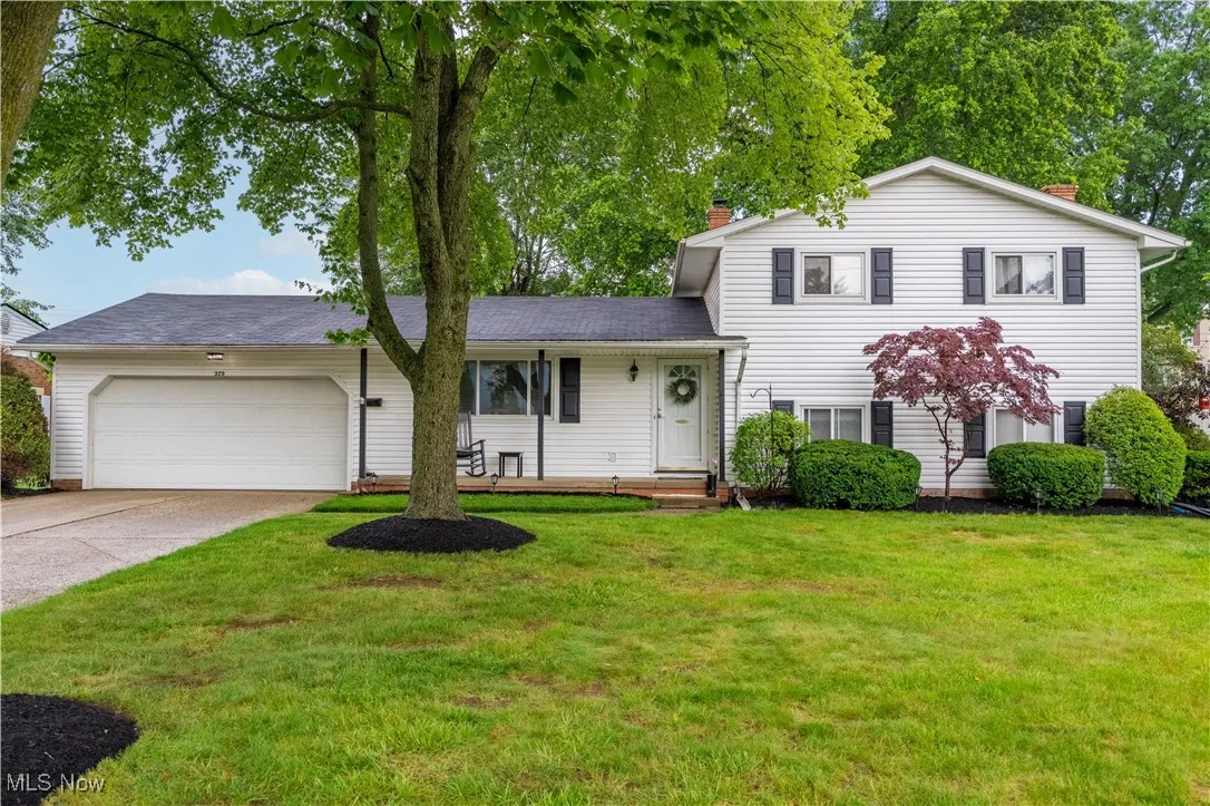 Split level home with an attached garage, driveway, front yard, and a porch