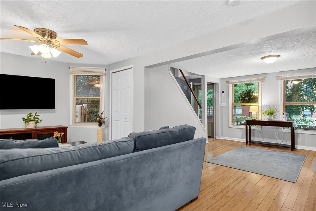 Living area with a textured ceiling, stairs, light wood-style floors, and a ceiling fan