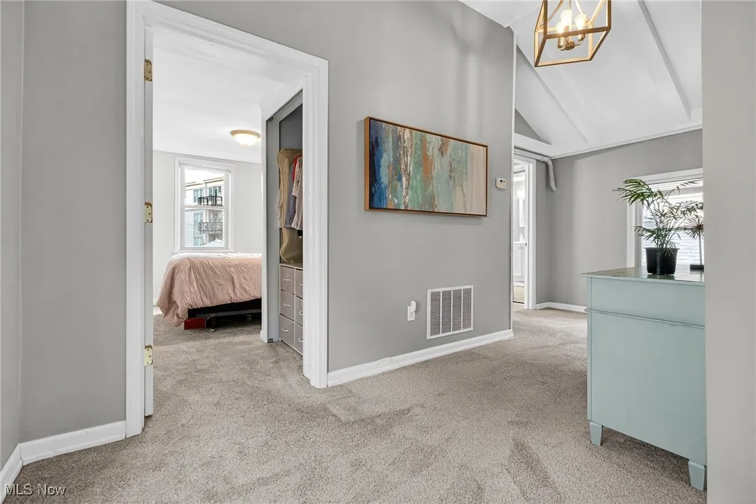 Corridor with carpet floors, a chandelier, and vaulted ceiling
