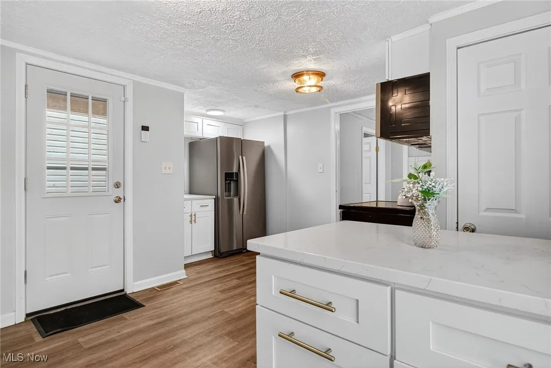 Kitchen with stainless steel refrigerator with ice dispenser, light wood-type flooring, ornamental molding, white cabinetry, and light stone counters