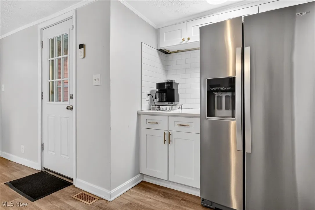 Kitchen featuring stainless steel fridge with ice dispenser, ornamental molding, light wood-style flooring, tasteful backsplash, and light countertops