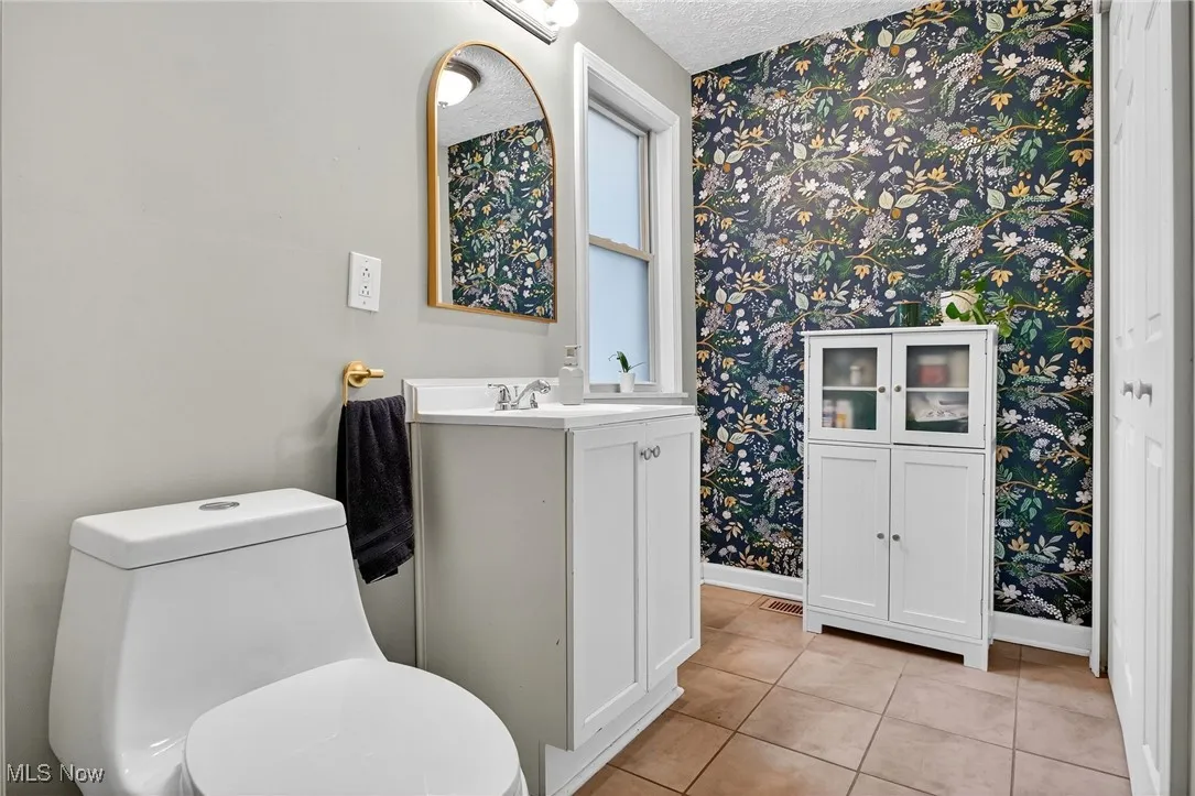 Bathroom featuring wallpapered walls, vanity, tile patterned floors, and a textured ceiling