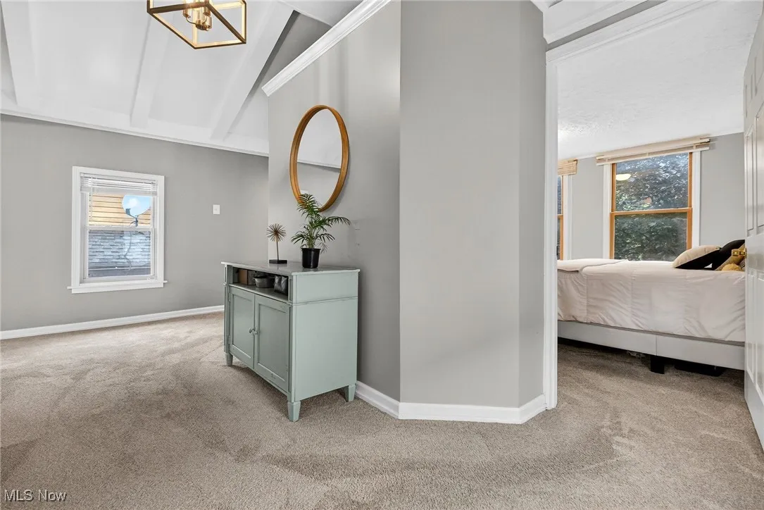 Hallway with light colored carpet, vaulted ceiling, and a chandelier