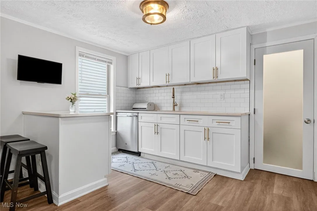 Kitchen with light wood-style floors, light countertops, backsplash, a textured ceiling, and crown molding