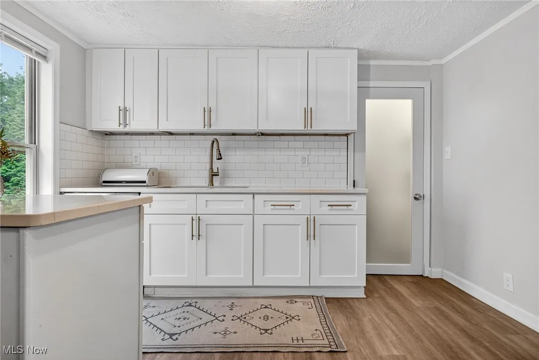 Kitchen featuring a textured ceiling, light countertops, white cabinetry, decorative backsplash, and crown molding