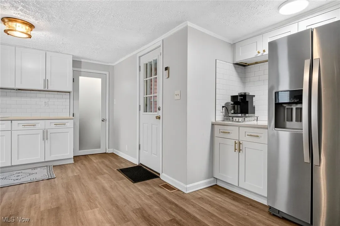 Kitchen with stainless steel fridge, light wood-type flooring, light countertops, a textured ceiling, and backsplash