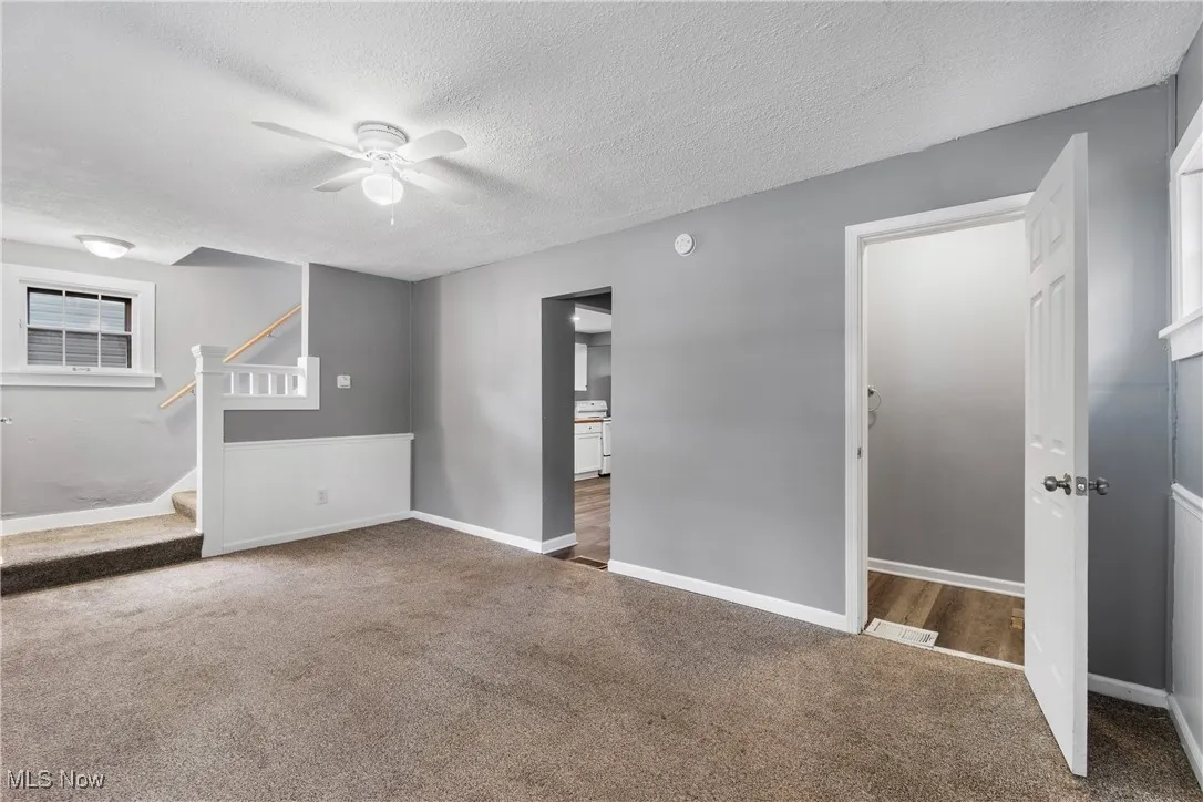 Carpeted living room with ceiling fan, stairway, and a textured ceiling