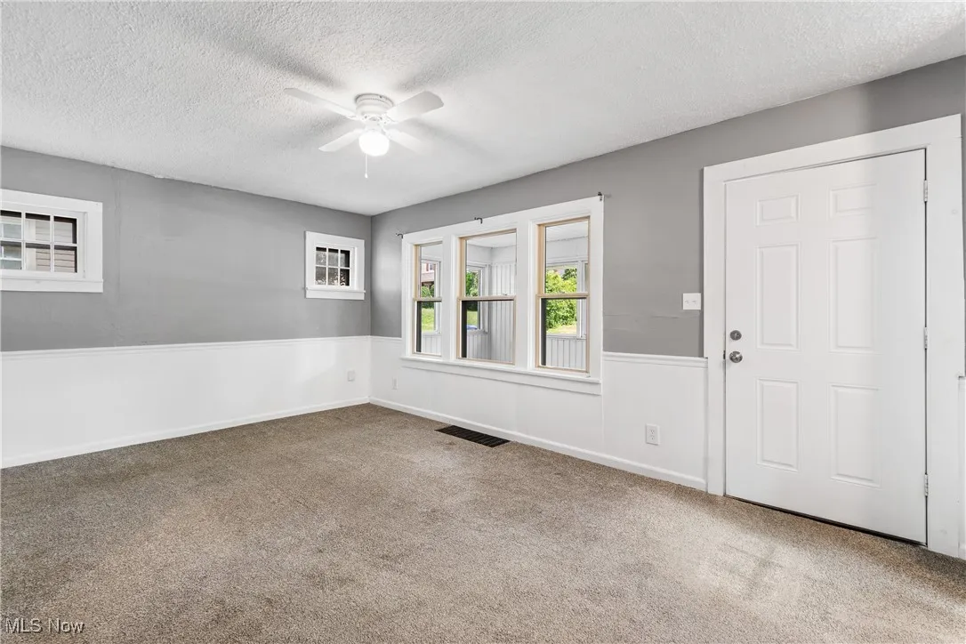 Carpeted living room with a textured ceiling, a ceiling fan, and a wainscoted wall