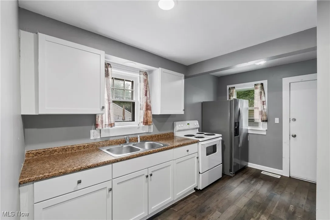 Kitchen featuring white electric range oven, white cabinets, dark wood-type flooring, and dark countertops