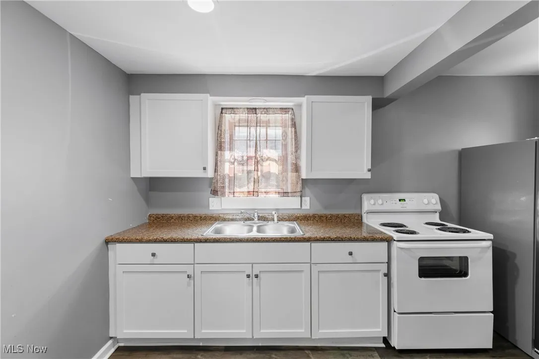 Kitchen with white electric range oven, white cabinetry, and freestanding refrigerator