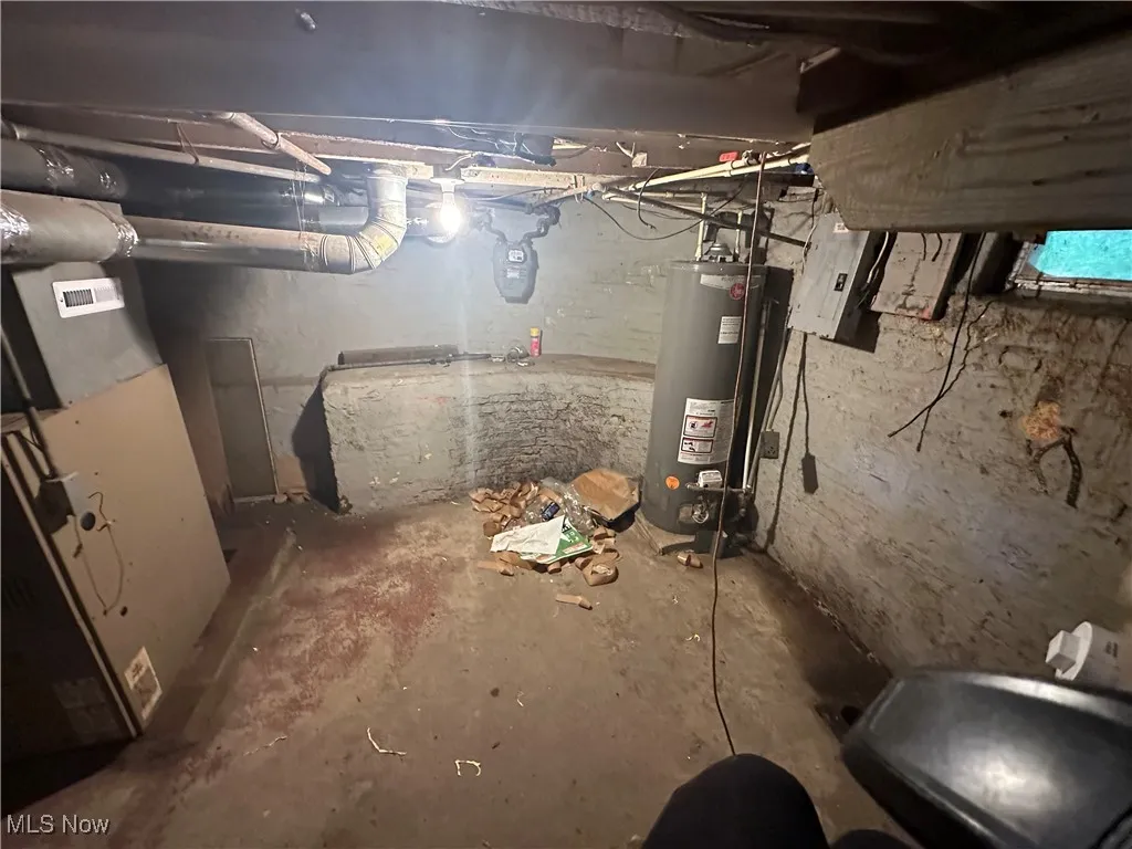 Unfinished basement with heating unit, gas water heater, and electric panel