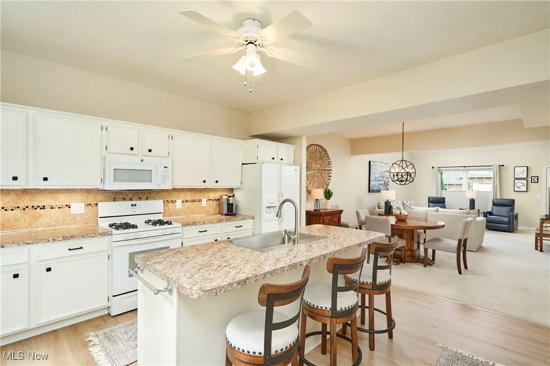 Kitchen with white appliances, light countertops, backsplash, open floor plan, and white cabinetry