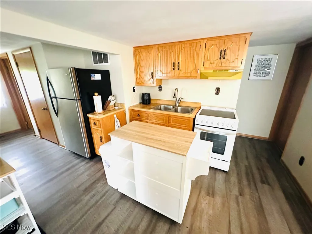 Kitchen with dark wood-type flooring, white electric range, freestanding refrigerator, and open shelves