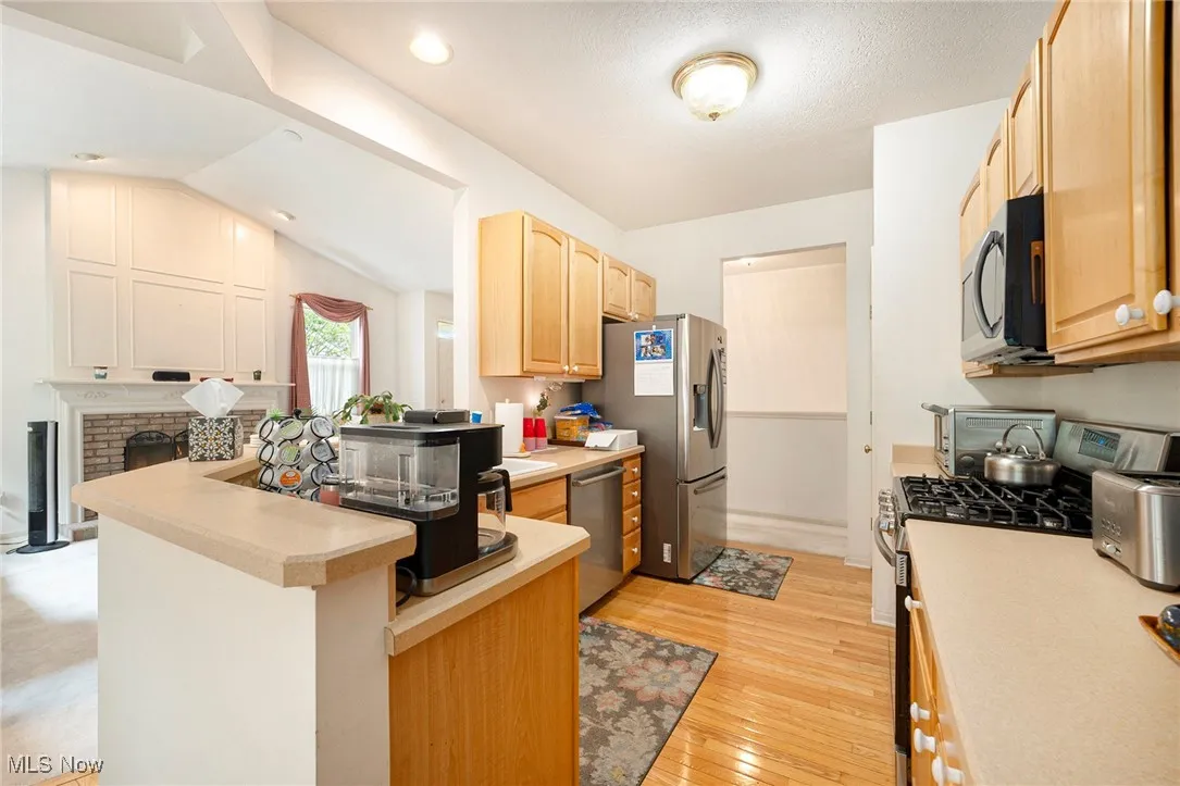 Kitchen featuring appliances with stainless steel finishes, light countertops, light wood flooring, a peninsula island