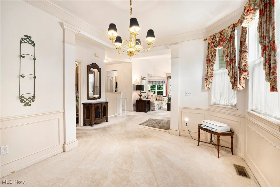 Hallway featuring a chandelier, crown molding, decorative columns, a decorative wall, and carpet flooring