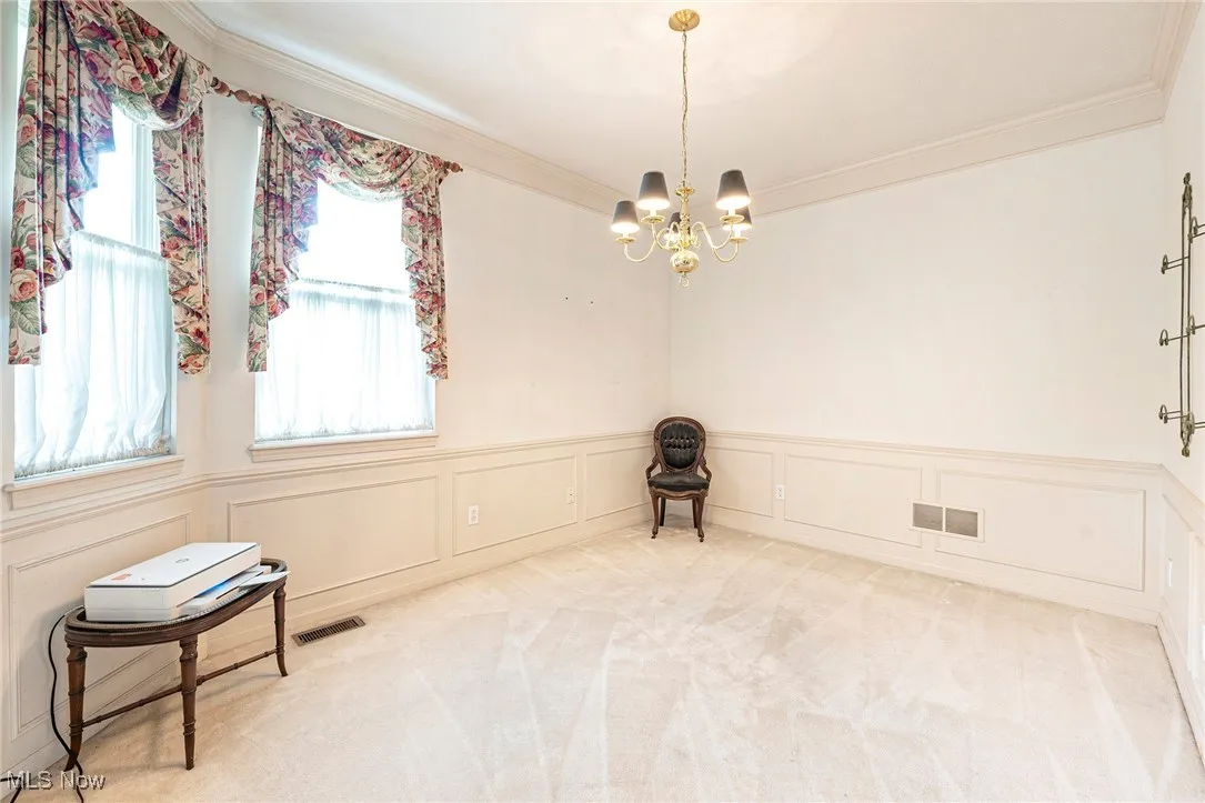 Carpeted empty room featuring a chandelier, ornamental molding, a decorative wall, and wainscoting