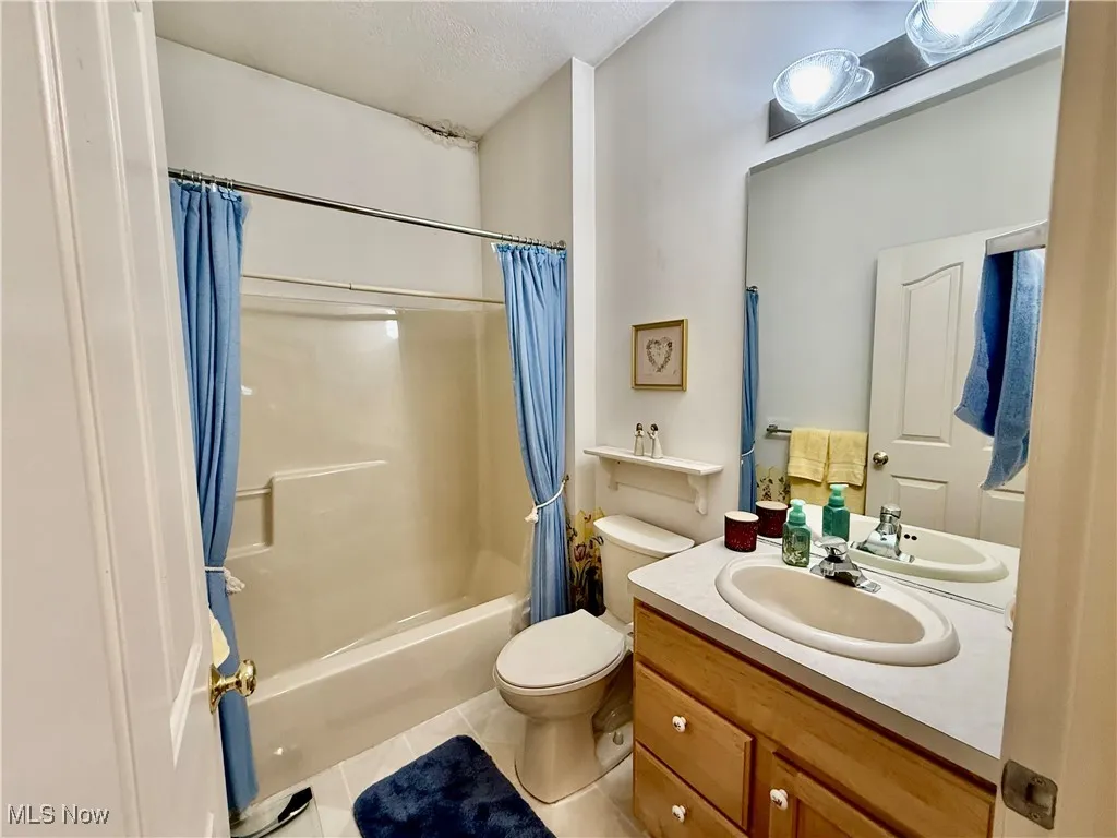 Bathroom with tile patterned flooring, shower / bath combo, vanity, and a textured ceiling