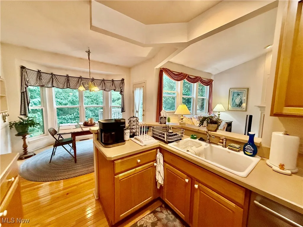 Kitchen featuring lofted ceiling, light countertops, brown cabinets, light wood-style flooring, and decorative light fixtures