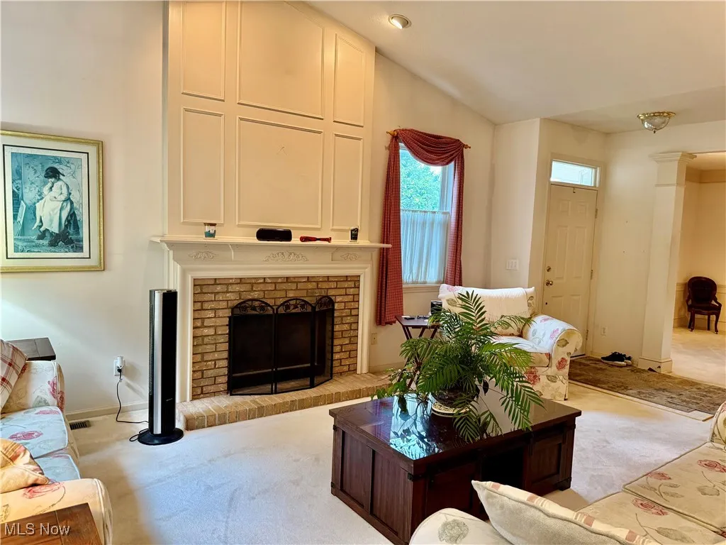Living room featuring carpet, a brick fireplace, and lofted ceiling