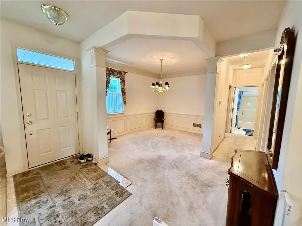 Carpeted foyer entrance with decorative columns, a chandelier, a decorative wall, and wainscoting