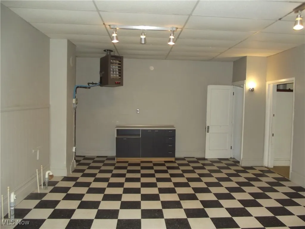 Basement featuring dark tile floors, a drop ceiling, and rail lighting