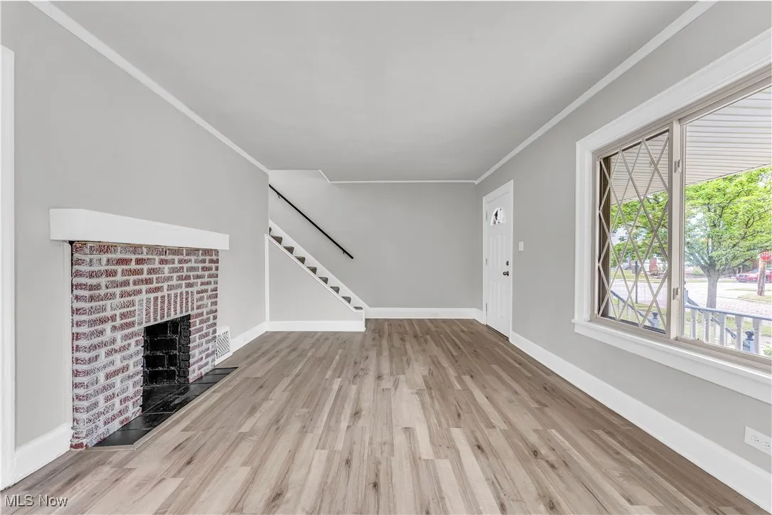 Unfurnished living room with crown molding, wood finished floors, a brick fireplace, and stairs