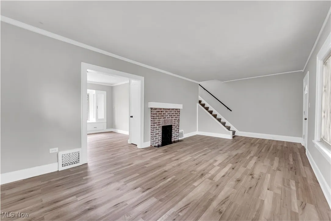 Unfurnished living room featuring a fireplace, wood finished floors, stairway, ornamental molding, and plenty of natural light