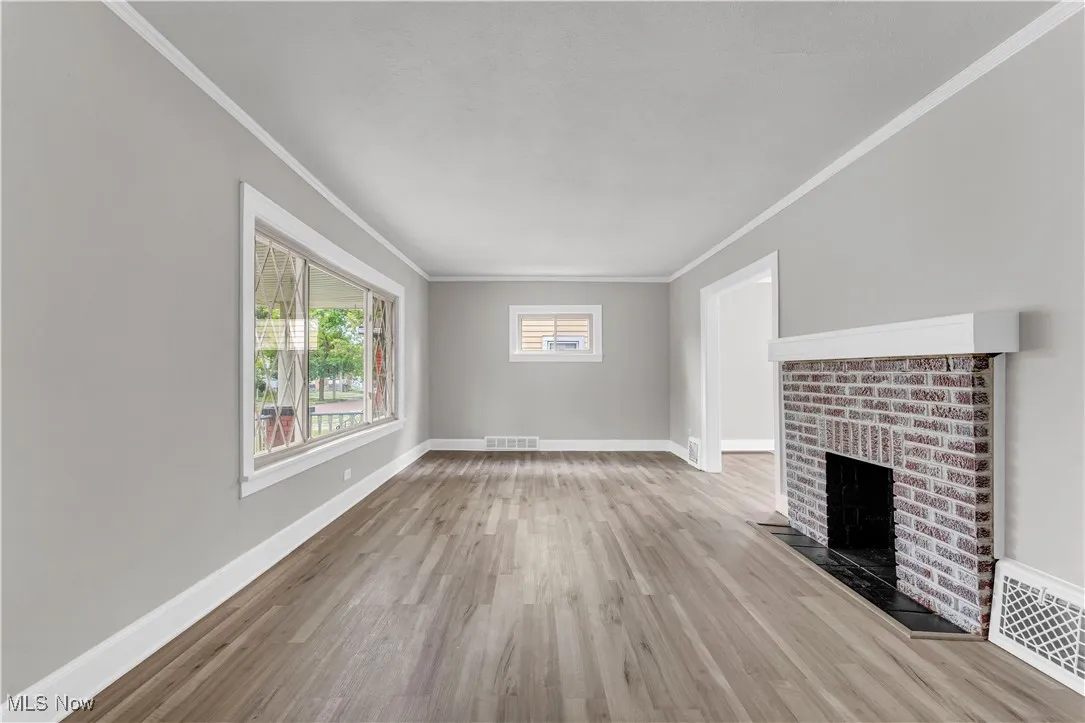 Unfurnished living room with ornamental molding, wood finished floors, and a fireplace