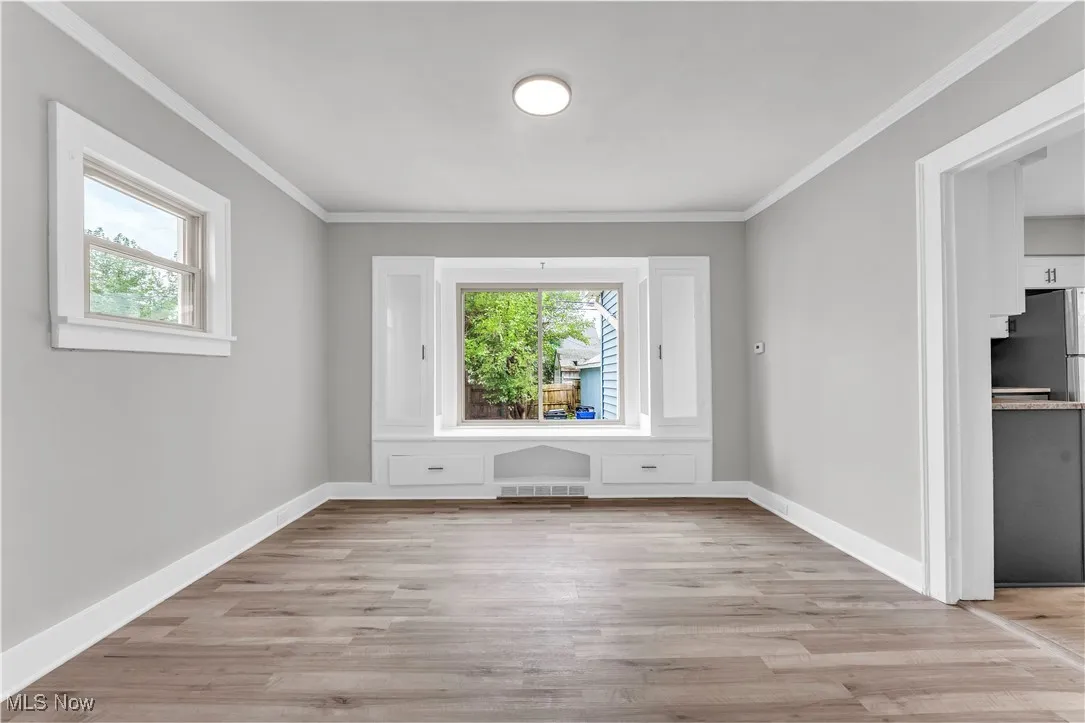 Spare room featuring healthy amount of natural light, light wood-style floors, and crown molding