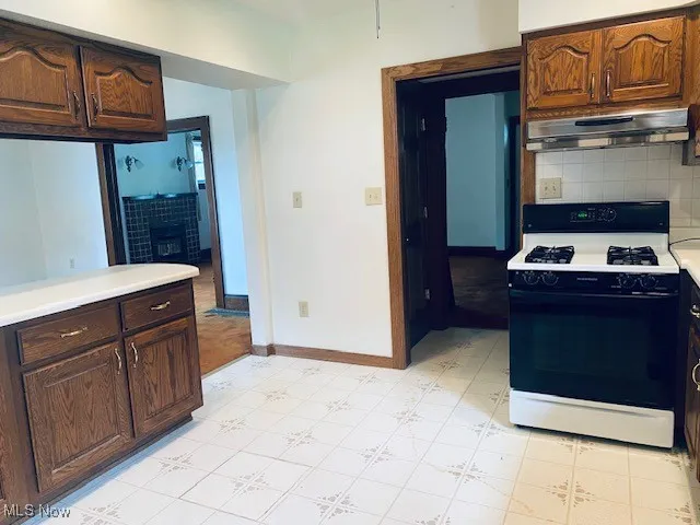 Kitchen with range with gas stovetop, under cabinet range hood, light countertops, tasteful backsplash, and light flooring