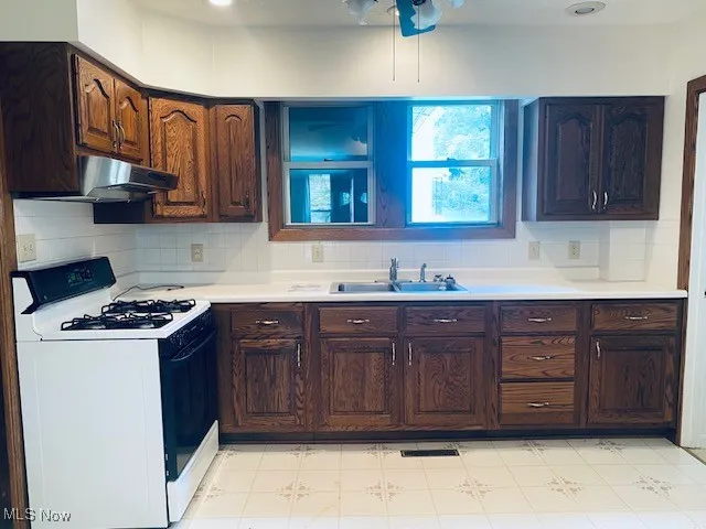 Kitchen featuring white gas range, light countertops, decorative backsplash, and dark brown cabinets