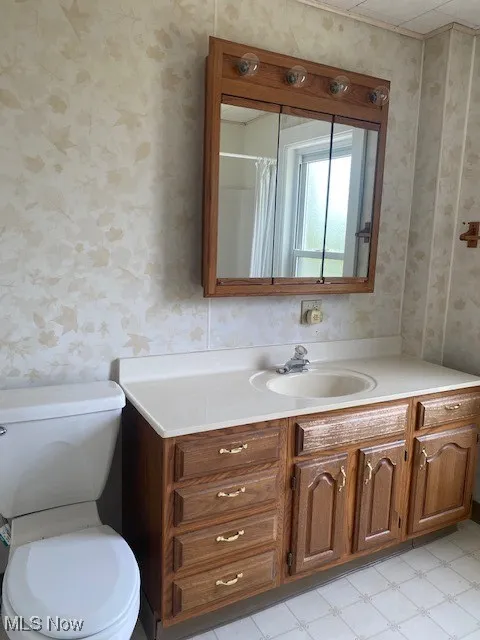 Full bathroom with wallpapered walls, vanity, and tile patterned floors