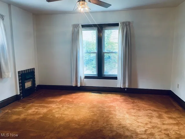 Unfurnished living room with carpet floors, ceiling fan, and a fireplace
