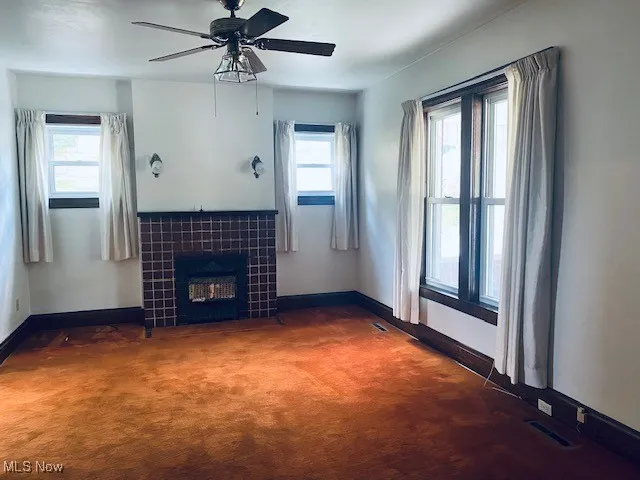 Unfurnished living room featuring carpet, plenty of natural light, a ceiling fan, and a tile fireplace