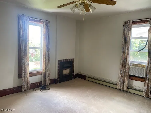 Unfurnished living room featuring a fireplace, carpet flooring, healthy amount of natural light, and a ceiling fan