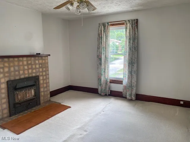 Unfurnished living room with a ceiling fan, carpet floors, a fireplace, and a textured ceiling