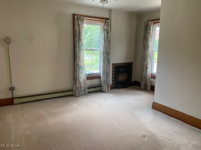 Unfurnished living room featuring healthy amount of natural light, carpet, and baseboard heating