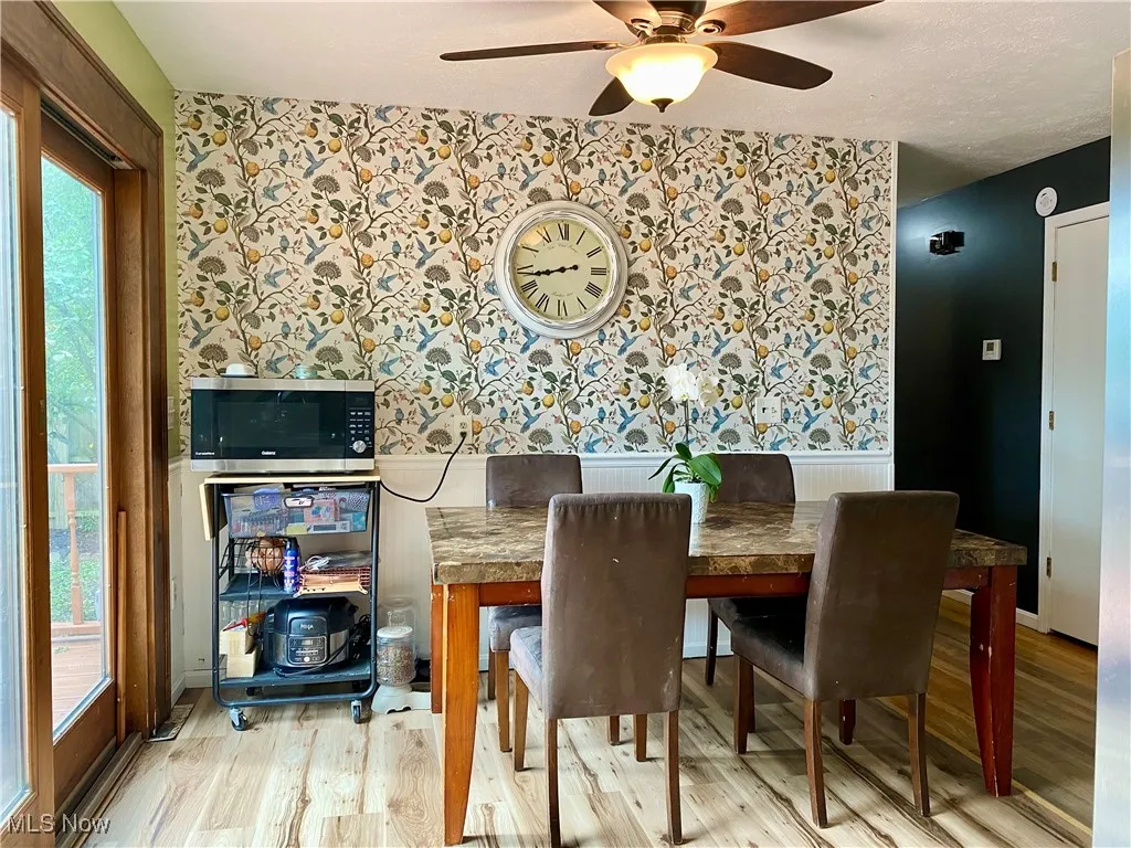 Dining area with wallpapered walls, light wood finished floors, and ceiling fan