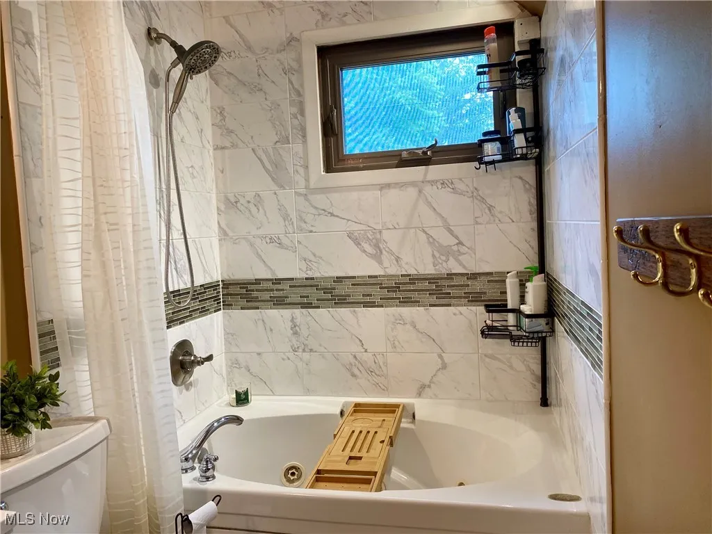 Bathroom featuring toilet and a combined bath / shower with jetted tub