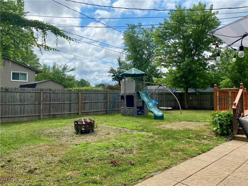 Fenced backyard featuring a playground and a fire pit