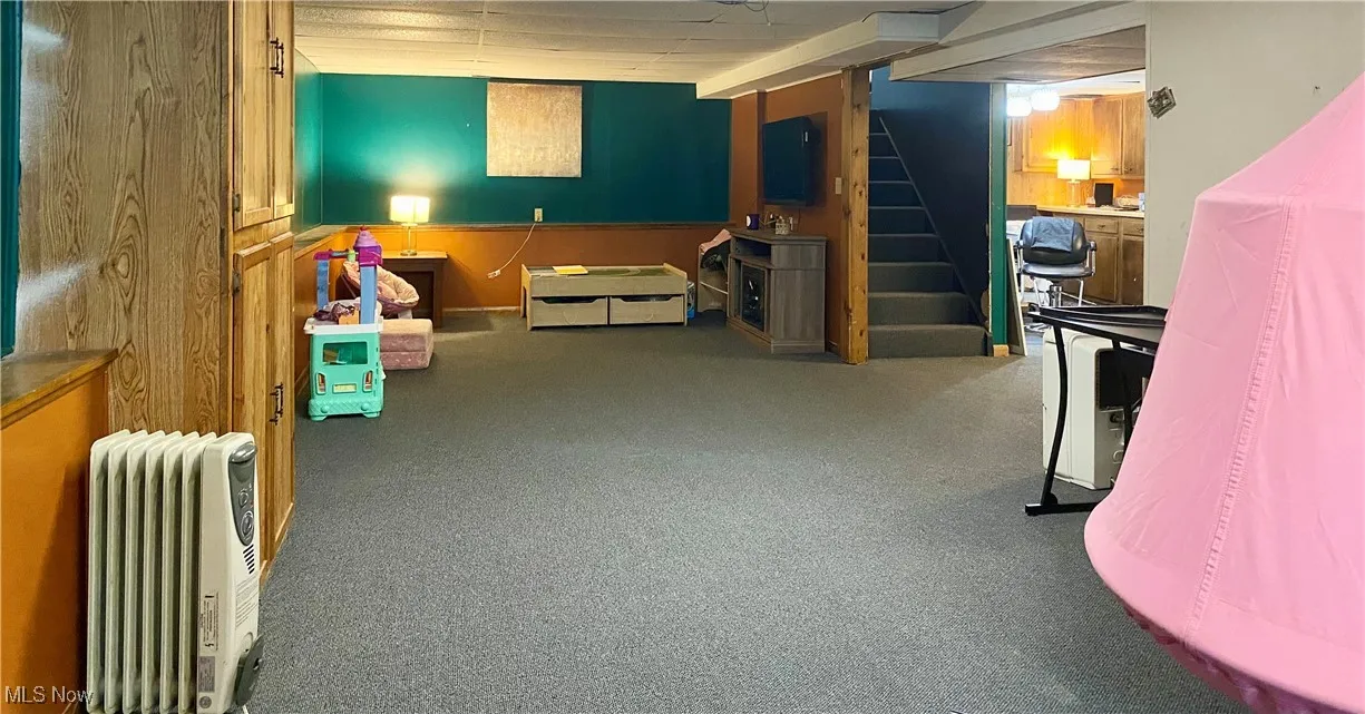 Living area with carpet floors, radiator, and stairway
