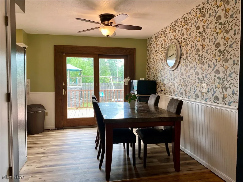 Dining space featuring a wainscoted wall, wallpapered walls, light wood-type flooring, and ceiling fan