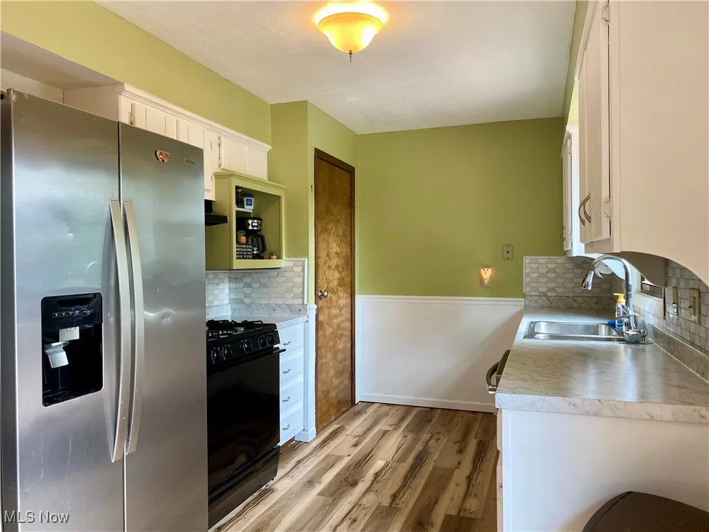 Kitchen featuring stainless steel fridge, gas stove, light countertops, light wood-type flooring, and white cabinetry