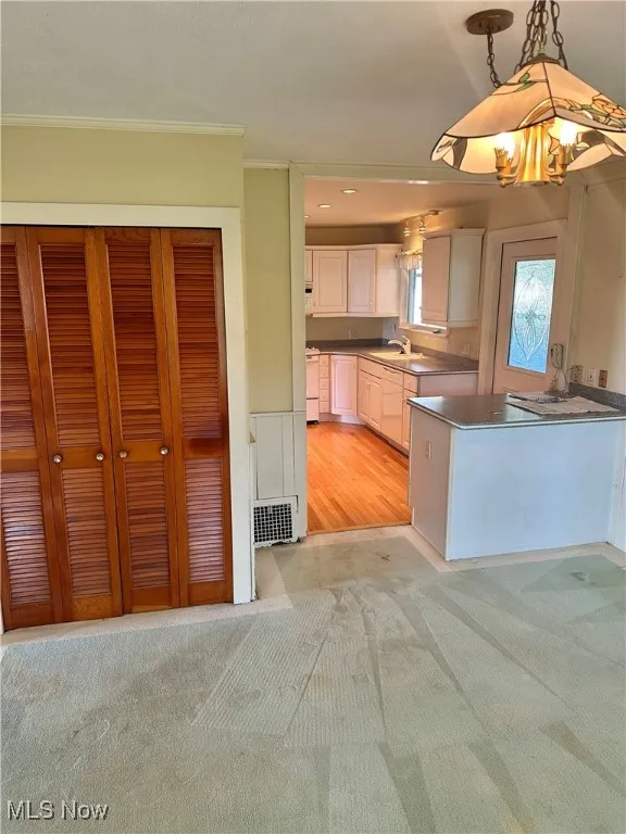Kitchen with light colored carpet, ornamental molding, decorative light fixtures, white cabinets, and dark countertops