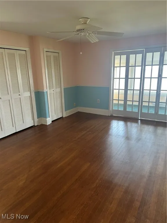 Unfurnished bedroom with dark wood-style flooring, multiple closets, and a ceiling fan